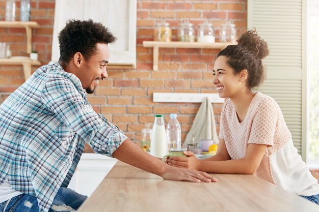 若いカップルや家族がキッチンで一緒に座って、楽しい話をし、牛乳を飲み、週末の計画について話し合う