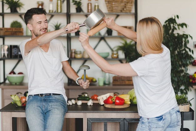 Young couple fighting with saucepan and rolling pin in the kitchen