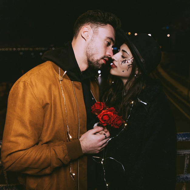 Free photo young couple in garland kissing in night street