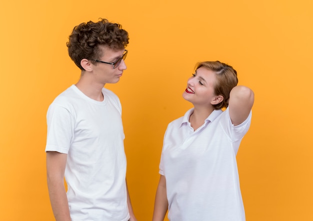 Young couple happy man and woman looking at each other smiling cheerfully standing over orange wall