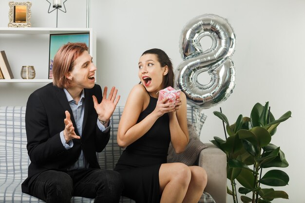 Young couple on happy women day holding present sitting on sofa in living room