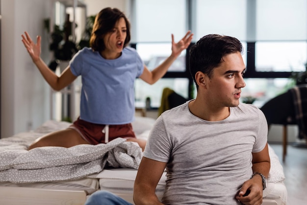 Бесплатное фото Молодая пара ссорится в спальне мужчина игнорирует свою девушку, которая кричит на него на заднем плане