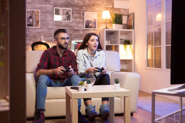 텔레비전에서 비디오 게임을 하는 동안 좋은 시간을 보내는 젊은 부부. 소파에 앉아 몇입니다.