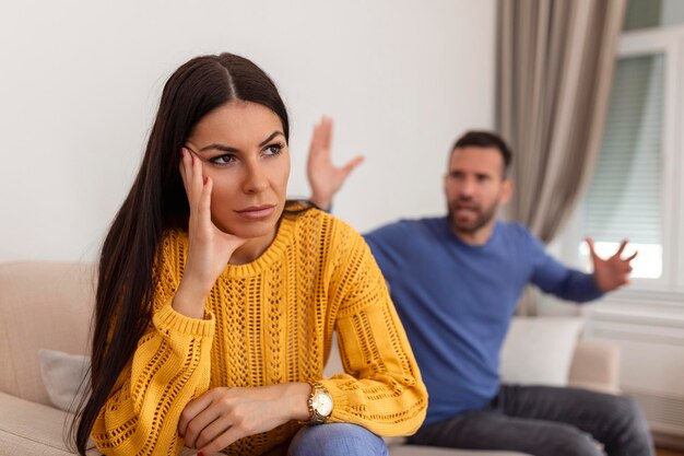 議論の対立を持っている若いカップル悪い関係怒っている怒りの女性怒っている若いカップルは、家族の戦いや喧嘩をしているリビングルームのソファに座って誤解に苦しんでいます