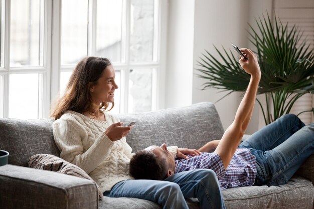 Young couple having fun with smartphones taking selfie at home