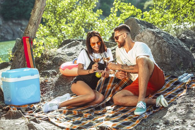 晴れた日に川沿いでピクニックをしている若いカップル。