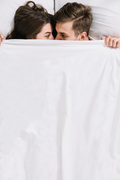 Young couple hiding under white blanket