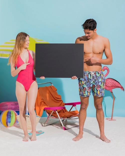 Free photo young couple holding dark blank card on beach