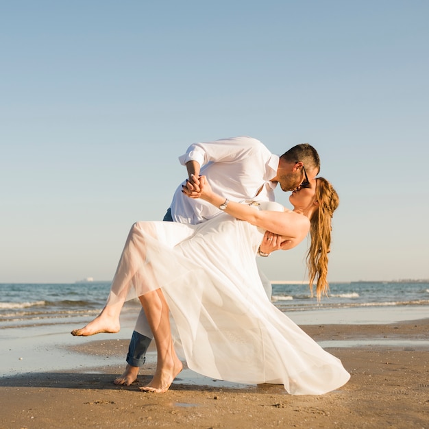 Young couple holding each other's hand giving pose while kissing at beach