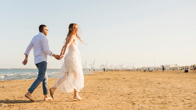 砂浜のビーチを走るお互いの手を握って若いカップル