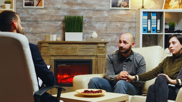 Young couple holding hands sitting on couch at couple therapy. Angry girlfriend.