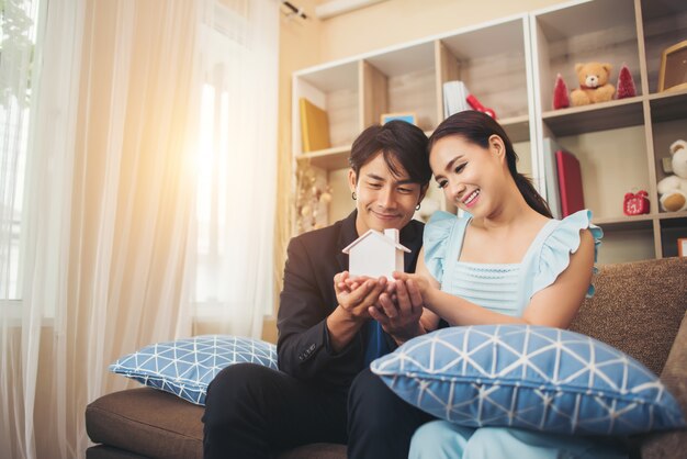 Young couple holding a white miniature house in living room