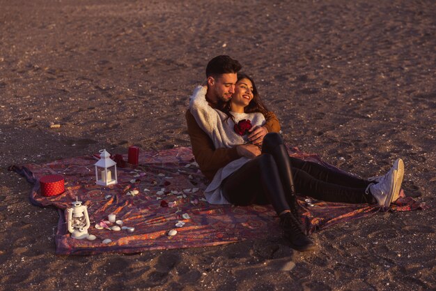 Young couple hugging on coverlet on sea shore 