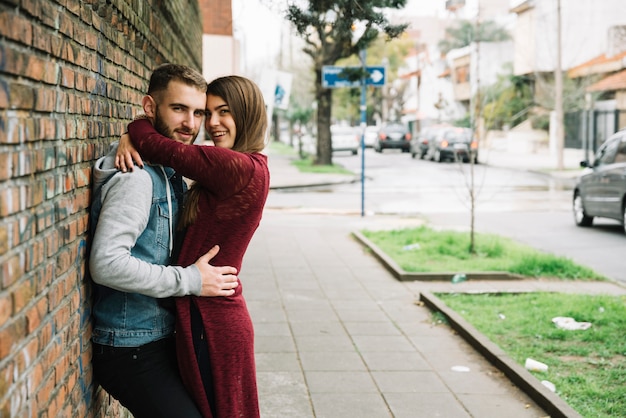 Young couple hugging in front of brick wall