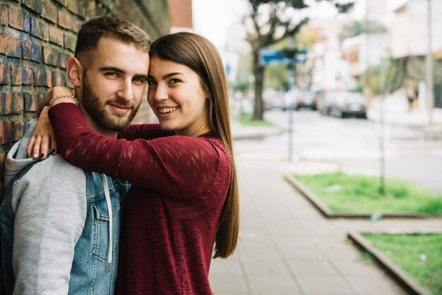 Young couple hugging in front of brick wall