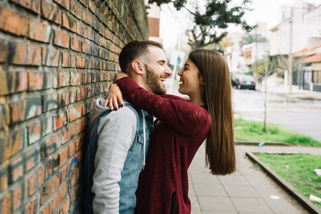 Free photo young couple hugging in front of brick wall