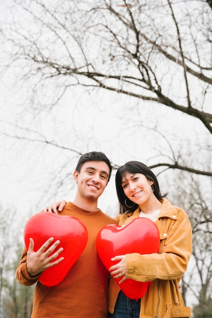 Free photo young couple hugging and holding heart shaped balloons