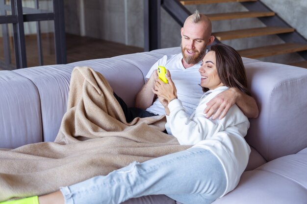 居心地の良い毛布の下のソファで自宅で若いカップルの夫と妻は、電話で自分撮りを取ります
