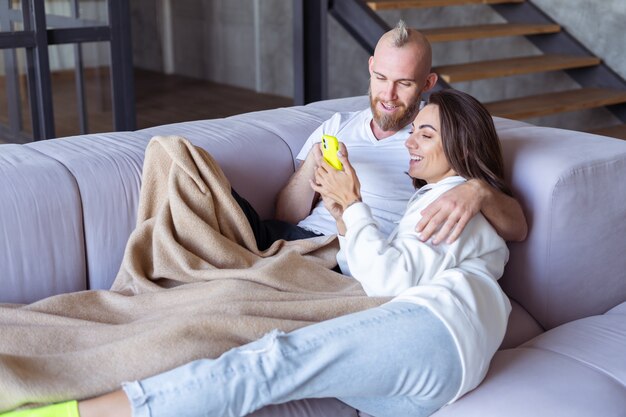 Young couple husband and wife at home on the couch under a cozy blanket, takes a selfie on the phone