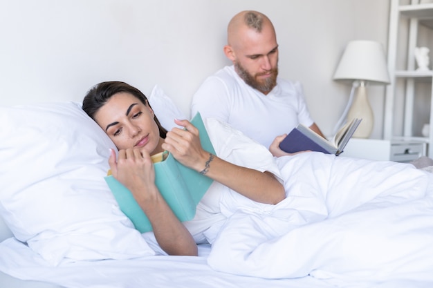 Молодая пара муж с женой дома в постели, читая книги осенним зимним вечером
