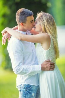 Молодая влюбленная пара собирается поцеловать, он держит ее за бедра, а она обнимает его за руки. одет в белое на зеленом фоне природы.