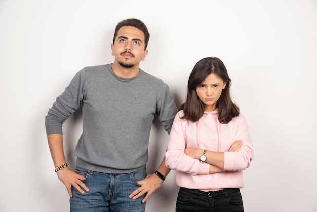 Young couple is mad at each other standing on white.