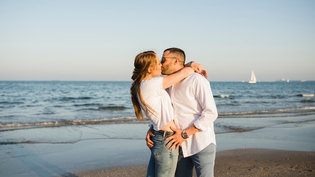 Молодая пара целует друг друга возле моря на пляже