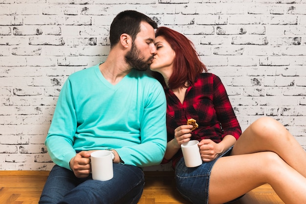 Young couple kissing each other while holding cup of coffee