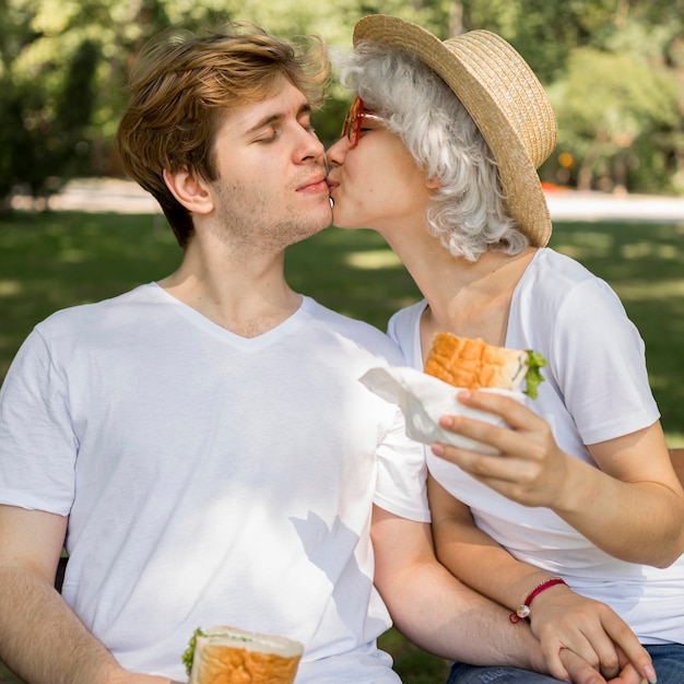 若いカップルがキスをし、公園でハンバーガーを楽しんで