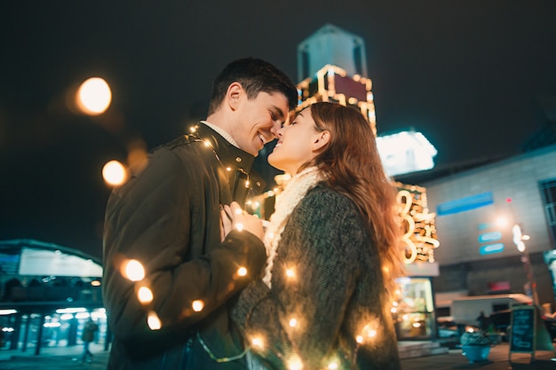 若いカップルがキスをし、クリスマスの時に夜の街で屋外を抱いて