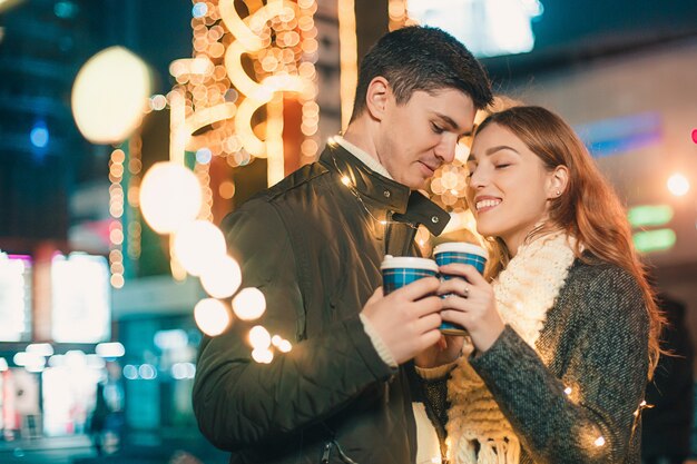 若いカップルがキスをし、クリスマスの時に夜の街で屋外を抱いて