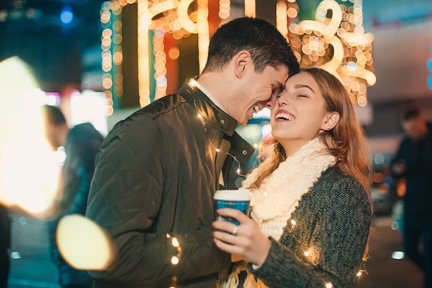 若いカップルがキスをし、クリスマスの時に夜の街で屋外を抱いて