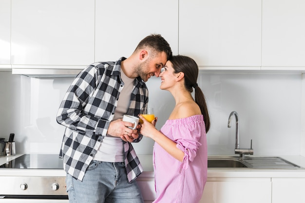 Young couple looking at each other holding cup of coffee and juice glass in kitchen