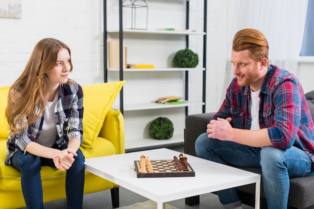 Free photo young couple looking at each other with chess board on the white table