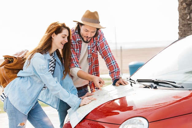 Young couple looking at road map on red car