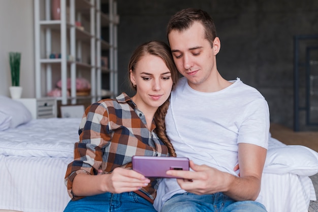 Young couple looking at smartphone near bed at home