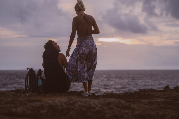 A young couple in love on a journey sits on the edge of a cliff and watches the sunset.