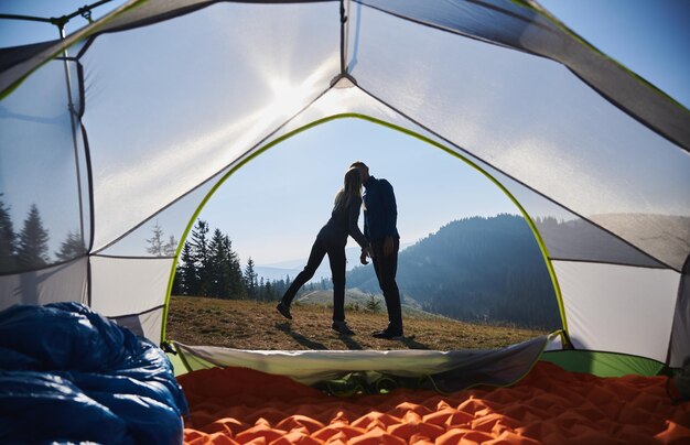 Молодая влюбленная пара целуется возле палатки лагеря