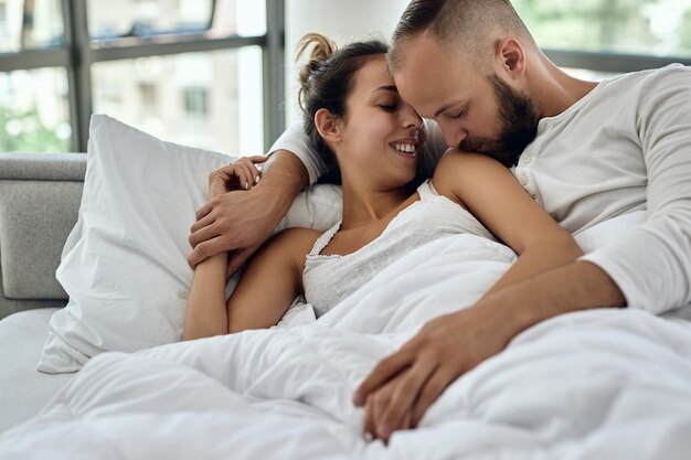 젊은 부부 사랑에 누워 침대에 포옹 남자는 어깨에 그의 여자 친구 키스