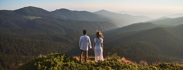 Young couple in love standing on grassy hill in mountains