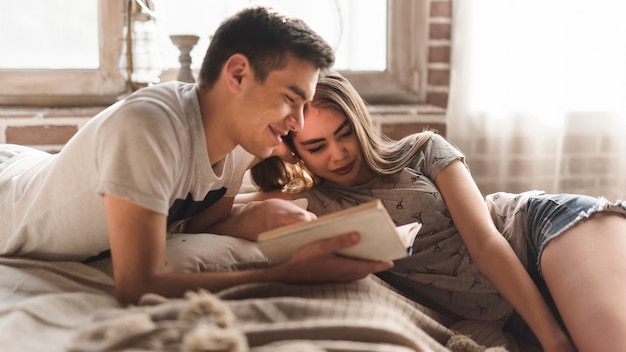 Young couple lying on bed looking at book