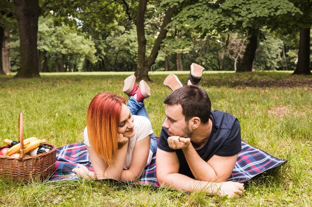公園でお互いを見て毛布に横たわっている若いカップル