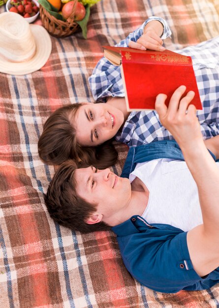 Young couple lying on blanket and reading book