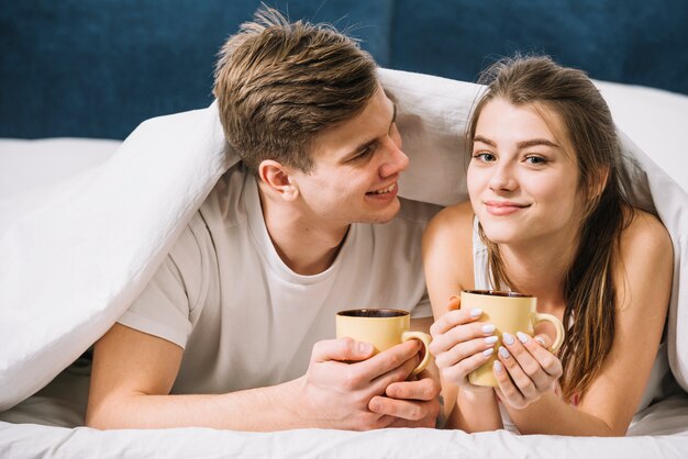 Young couple lying under blanket with coffee