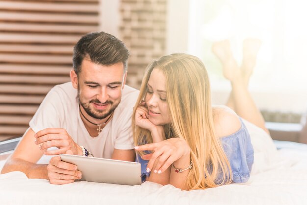 Young couple lying on cozy bed looking at digital tablet