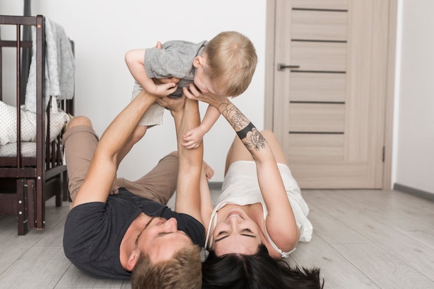 Free photo young couple lying on hardwood floor holding their son on hands