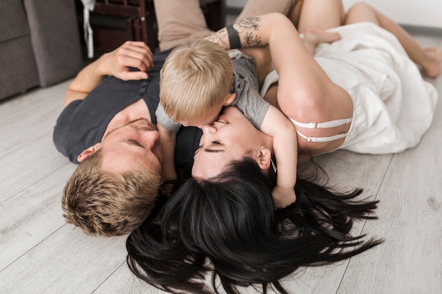 Foto gratuita giovane coppia sdraiata sul pavimento in legno giocando con il loro figlio