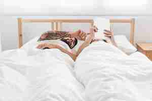 Бесплатное фото Молодая пара, лежа на кровати, используя цифровой планшет