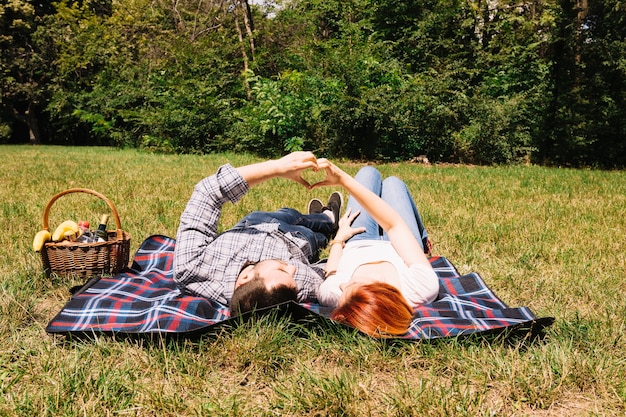 무료 사진 손으로 하트를 만드는 푸른 잔디 위에 담요에 누워있는 젊은 부부