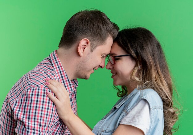 Young couple man and woman in casual clothes happy in love hugging having fun together standing over green wall